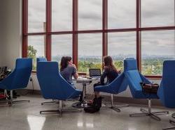 Two students sitting in the School of Communication and Media on their laptop discussing something.